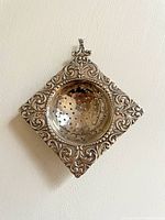 Front view of the diamond shaped sterling silver tea caddy strainer showing intricate embossed scrollwork and perforated bowl.
