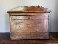 Full front view of the antique wooden storage cabinet showing scalloped top edge and front panel with knob.