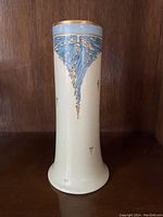 Front view of the vase showing handpainted blue leaves and gold accents on cream ceramic with a flared base.