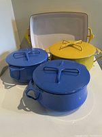 Three round enameled pots (two blue, one yellow) and one yellow rectangular casserole dish arranged on countertop