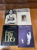 Four books including James Taylor, Gordon Lightfoot, Motown Era, Bob Dylan sheet music on wooden floor.