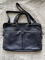 Front of the blue leather satchel tote showing pebbled texture, front zippered pocket with two zipper pulls, and double handles.