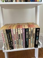 Photo of 19 Isaac Asimov paperback books arranged on a white shelf showing titles and varying spine colors.