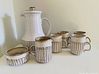 Full set with teapot, four cups, cream pitcher, sugar bowl arranged on white surface against corner background.