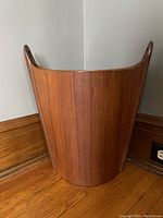 Front view of the teak garbage pail showing smooth wood grain and curved form with cut-out handles.