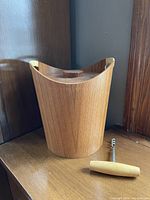 Front side view of teak ice bucket with lid and vintage corkscrew beside it on a wooden surface.