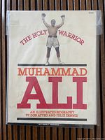 Front cover of the biography book showing Muhammad Ali with gloves raised and title in large red font.