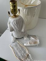 White ceramic rabbit lamp base with gold colored bulb socket and harp, some parts still in plastic packaging, sitting on a white table.