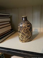 Glazed faience vase showing full body with black and yellow glazed abstract decoration.