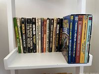 A shelf with 16 Robert Heinlein paperback books of mostly vintage editions with varying spine colors and fonts, some worn, including titles such as Tunnel in the Sky and The Number of the Beast.
