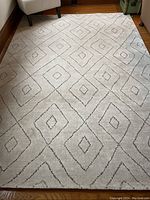 Full top-down view of the rectangular rug displaying the diamond patterned design in gray on light beige/off-white background on a hardwood floor