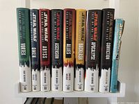Photo showing nine hardcover Star Wars Fate of the Jedi series books plus one older Star Wars book by George Lucas, arranged side by side on a white bookshelf.
