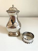 Front view of sterling silver pepper shaker and napkin ring showing shape, finish and details.
