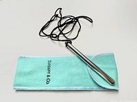 Photo showing the sterling silver Tiffany & Co Elsa Peretti pen resting on the light turquoise Tiffany & Co pouch with a black cord attached to the pen.
