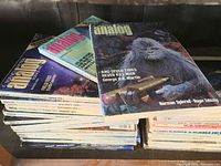 Close-up stack of Analog Science Fiction magazines, showing colorful covers and titles with author names including George R. R. Martin and Roger Zelazny.