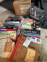 Overview photo showing the Craftsman Dual Action electric sander next to multiple unopened and opened packs of sandpaper sheets of various types and grits.