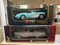Two boxed 1:18 scale die cast cars stacked: turquoise 1957 Chevrolet Corvette on top and silver 1957 Ford Thunderbird below