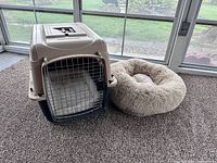 Front view of beige and black Petmate dog crate next to plush dog bed