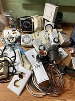 Wide view of electrical supplies showing multiple timers, outlets, switches, wall plates, wiring, and electrical tape arranged on a wooden surface.