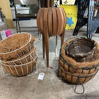Overview of lot showing white metal hanging baskets with coconut liners, black woven basket and mid-century modern wooden planter with legs.