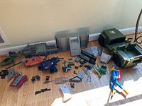 Overview of various GI Joe vehicle parts, figures and accessories spread on floor. Includes green jeep, red boat, blue buggy and blue diver figure with yellow fins.