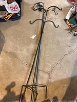 Three black iron shepherd's hooks laid on a garage floor showing the full length with rectangular ground stakes and double hooks at the top.