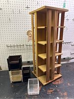 Photo showing full view of wooden 4-sided rotating storage shelf with plastic bins beside it on a workbench with pegboard background.