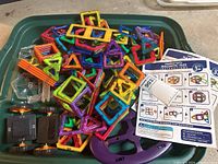 Photo showing a large pile of colorful magnetic tiles in various shapes including squares and triangles, plus a printed instruction sheet on the tray.