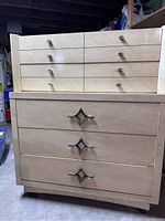 Front view of the chest showing three large drawers with diamond-shaped metal pulls and the upper section with smaller drawers and round knobs, made of light wood.