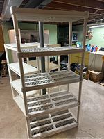 Front angled view of a white plastic shelving unit with five vented shelves in a basement environment.