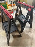 Two black SKIL saw horses with red ruler tops standing on concrete floor.