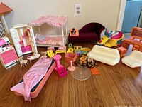 Wide view of all vintage Barbie furniture and accessories on hardwood floor showing beds, seating, kitchen units, and small pieces.