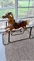 Full side view of the vintage Wonder Horse spring rocking horse toy, showing its cream mane, brown plastic body, and metal spring base on carpeted floor near windows.