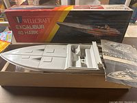 Box and boat hull of Wellcraft Excalibur 40 Hawk beside its box with colorful branded graphics.