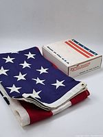 Folded vintage cotton American flag alongside original box with 'Made in the U.S.A.' text and flag imagery.