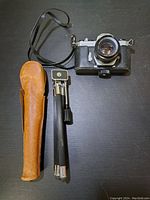 Top-down view of camera with attached lens, tripod folded beside it and tripod case to left, showing all items included
