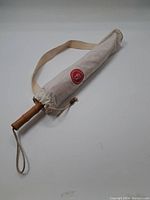 Full umbrella in beige fabric carrying sleeve with strap and wooden handle visible at one end.