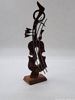Front angle view of carved wooden abstract musical sculpture showing metal strings and base.