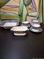 View of the full set of Copeland Spode Battersea dinnerware pieces including serving dishes, cups, saucers, and plates on a black surface.