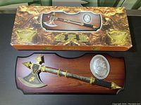 Photo of the boxed decorative battle axe mounted on a wooden plaque with silver medallion.