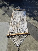 Full view of the cotton rope hammock laid out on concrete showing entire length and wooden spreader bars at both ends.
