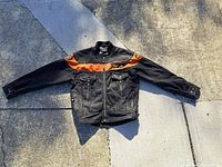Full view of black and orange Harley Davidson motorcycle jacket laid flat showing front, sleeves, collar, and pockets.