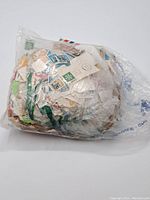 Full view of large bag containing assorted postage stamps with many attached to paper pieces.