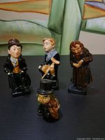Front view of four Royal Doulton porcelain figurines placed on a black surface with a colorful background, showing details of the faces and clothing of each character.