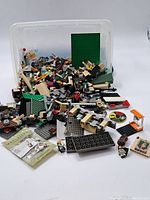 Full view of assorted LEGO pieces spilling out of plastic container on white background.