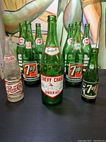 Front view of the vintage soda bottles including 7-Up, Chevy Chase Ginger Ale, Pepsi-Cola, and Frostie bottles arranged on a table.