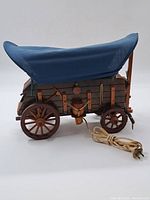 Side and angled view of wooden model horse carriage with blue fabric canopy and attached electric cord.