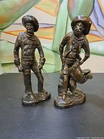 Front view of two bronze cowboy figures showing detailed clothing and facial features with ropes.