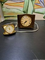 Pair of vintage clocks on black surface, one electric wood Westclox clock and one small folding travel clock.