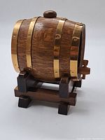 Front angled view of small wooden barrel with brass bands on wooden stand